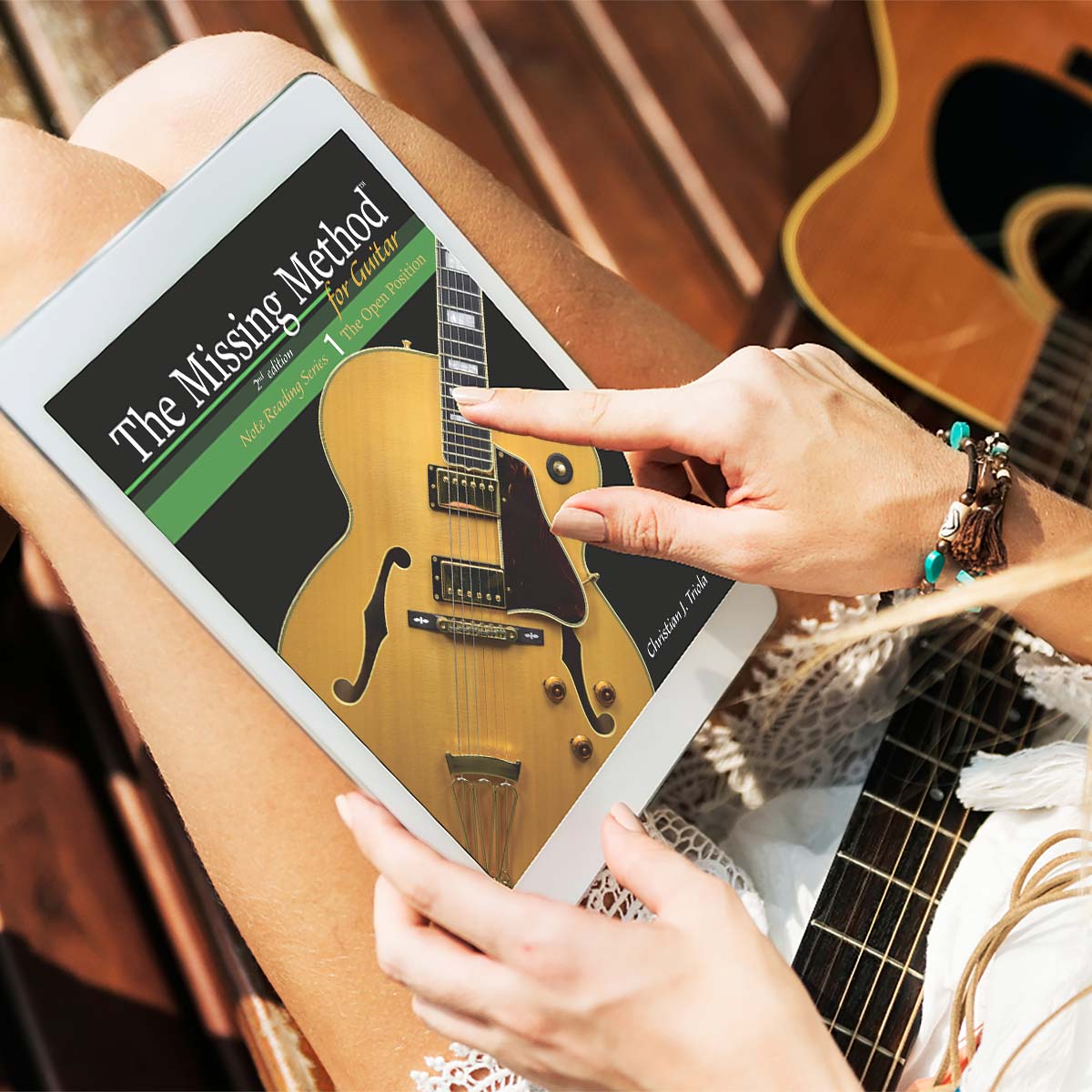 Woman with guitar and The Missing Method for Guitar Note Reading Series Book 1 on a digital tablet